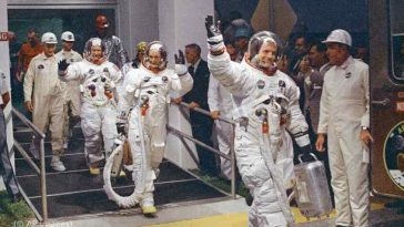 نيل أرمسترونج ، يلوح في المقدمة ، يتجه نحو الشاحنة التي ستقل الطاقم إلى الصاروخ لإطلاقه إلى القمر