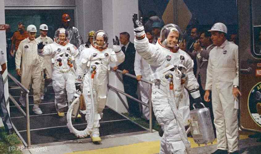 نيل أرمسترونج ، يلوح في المقدمة ، يتجه نحو الشاحنة التي ستقل الطاقم إلى الصاروخ لإطلاقه إلى القمر